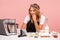 Smiling cooker in apron posing near table with ingredients for pastry and food processor, baker looking at tablet screen,