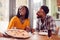 Smiling Couple On Date In Restaurant Together With Waiter Holding Pizza In Foreground