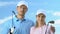 Smiling couple of golfers posing with clubs against blue sky, golf club trainers