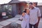 Smiling Couple Standing Outdoors In Front Of House With For Sale Sign In Garden Holding Keys