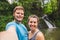 Smiling couple taking selfie in front of waterfall in woods