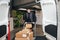 Smiling courier in uniform standing in warehouse with cart preparing for delivery