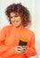 Smiling curly haired woman in neon orange hoody drinks coffee outdoors