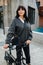 Smiling cute black-haired woman tugging ebike, walking on the street