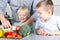 Smiling cute daughter and son cooking a dinner. Little children chopping a colorful pepper with father.