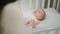 Smiling cute little baby girl very excited hugging hands of her mother while is laying down on the baby cot