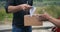 Smiling delivery man in strict dark-grey shirt delivering parcel box to recipient - courier service concept