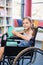 Smiling disabled school girl on wheelchair holding a books in library