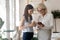 Smiling diverse female colleagues enjoy coffee break with cellphone