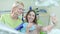 Smiling doctor and patient taking selfie in dentist office. Woman showing v-sign