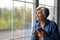 Smiling dreamy mature woman holding phone, looking out window