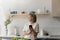 Smiling dreamy older mature woman using cellphone in kitchen.