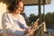 Smiling elder caucasian woman using a smart phone on the balcony of her house