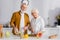 Smiling elderly couple cooking fresh salad near wine and baguette in kitchen.