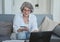 Smiling elderly female bank client making quick online payments with her credit card and laptop