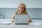 A smiling elderly woman using a laptop and looking at the camera. A business woman uses her laptop.