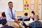 Smiling elementary school teacher sitting on a pupilï¿½s desk