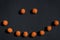 Smiling emoticon made from orange fluffy pom-poms on a black background. Halloween festive background.Top view, flat lay