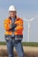 Smiling engineer with hard hat and protective clothing in front of a windmill