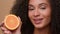 Smiling ethnic model girl African American woman hold half healthy orange fruit shake head with curly hair curls