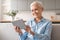 Smiling european mature lady holding digital tablet relaxing at home