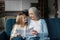 Smiling european small girl gives card to old woman, enjoy moment together in living room interior