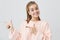 Smiling fair-haired young woman in pink sweatshirt pointing at copy space for your advertisment or text. Positive girl