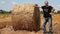 Smiling Farmer Leaning on Hay Bale In Agriculture Field
