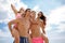 Smiling fellows in swimming trunks holding beautiful girls on a seashore on a blurred natural background.