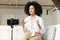 Smiling female African American blogger influencer sitting at phone on stabilizer