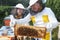 Smiling female apiarist by male beekeeper holding honeycomb frame