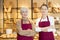 Smiling female bakers in maroon aprons standing with crossed arms