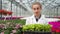 Smiling female biology researcher walking in greenhouse holding box with plants looking at camera