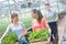 Smiling female botanists talking while carrying plants against male coworker in greenhouse