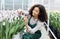 Smiling female darkskinned greenhouse worker checks condition of seedlings