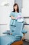 Smiling Female Dentist Standing By Dental Chair At