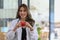 Smiling female doctor in white uniform standing in medical office and holding red heart.