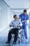 Smiling female nurse pushing and assisting patient in a wheelchair in the hospital