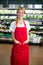 Smiling female staff standing with hands in pocket in grocery section