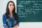 Smiling female teacher standing in front of blackboard in classroom