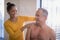 Smiling female therapist giving neck massage to shirtless senior male patient at hospital ward