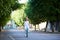 Smiling female in white dress and straw hat riding blue bike dow green wide city street