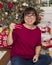 Smiling fifty-eight year old Korean woman in front of a Christmas tree and presents