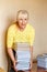 Smiling fifty-year-old woman librarian in a yellow jacket raises a large stack of identical books