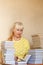 Smiling fifty-year-old woman in a yellow sweater reading a book. home library