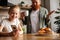 Smiling freckled child using smartphone near blurred angry father during breakfast in kitchen, parenting struggles concept