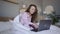 Smiling freelancer with laptop and notepad in bed
