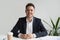 Smiling friendly millennial businessman sitting at desk looking