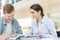 Smiling friends discussing over book while sitting at table in library