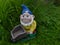 Smiling garden dwarf with a blue hat, yellow jacket and a wheelbarrow on a green meadow
